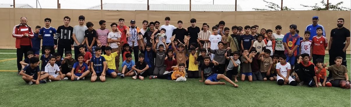 Large group photo of kids and coaches on the turf pitch at Zaatari camp
